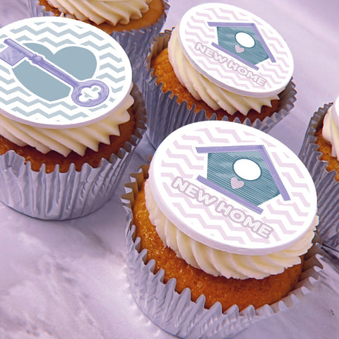 Frosted cupcakes topped with a new home icing decoration featuring a lavender and teal house design, one with a key icon and one with the words "NEW HOME.".