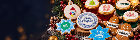 Display of branded Christmas treats including snowflake biscuits, logo cupcakes, branded gingerbread men and bauble biscuits on a festive table. 