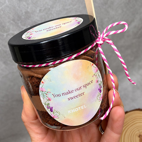 Hand holding a branded cake jar with a pastel logo sticker and wooden spoon