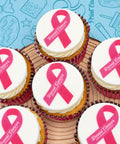 Breast Cancer Awareness Month branded cupcakes in pink cases with a pink ribbon design, on a wooden board