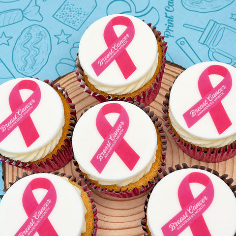 Breast Cancer Awareness Month branded cupcakes in pink cases with a pink ribbon design, on a wooden board