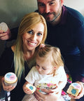 A family doing a gender reveal with cupcakes. A mother and father are shown with a toddler, all holding a cupcake.