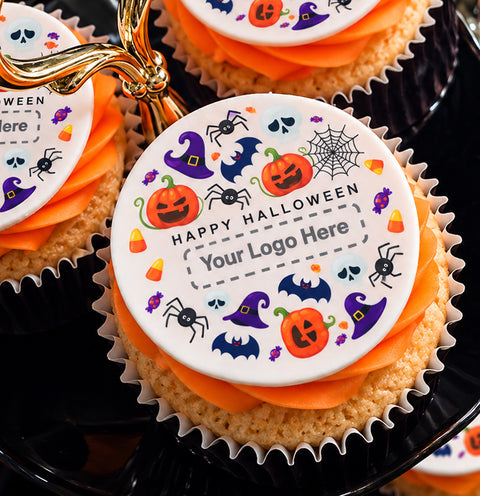Close-up of Halloween-themed cupcakes with toppers on orange-frosted cupcakes, featuring pumpkin, witch hat, spider, bat, spiderweb, candy corn, and the text 'Happy Halloween' with a customisable logo area.