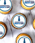 Overhead view of International Men's Day cupcakes with blue tie design toppers on marble table for office event