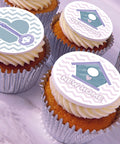 Frosted cupcakes topped with a new home icing decoration featuring a lavender and teal house design, one with a key icon and one with the words "NEW HOME.".