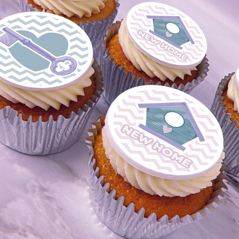 Frosted cupcakes topped with a new home icing decoration featuring a lavender and teal house design, one with a key icon and one with the words "NEW HOME.".
