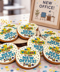 Iced biscuits reading "Welcome to your new office" arranged on a wooden stand beside a framed new office illustration