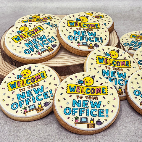 Round sugar cookies decorated with a fun 'Welcome to Your New Office!' design, arranged on a rustic wooden slice and a light grey surface.