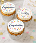 Personalised congratulations cupcakes  on a marble surface, each topped with a round icing decoration that reads Congratulations! 