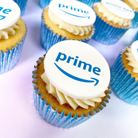 Branded cupcakes with amazon prime logo printed onto the icing disc. They are baked in a light blue case with vanilla sponge showing and the buttercream piped swirl. 